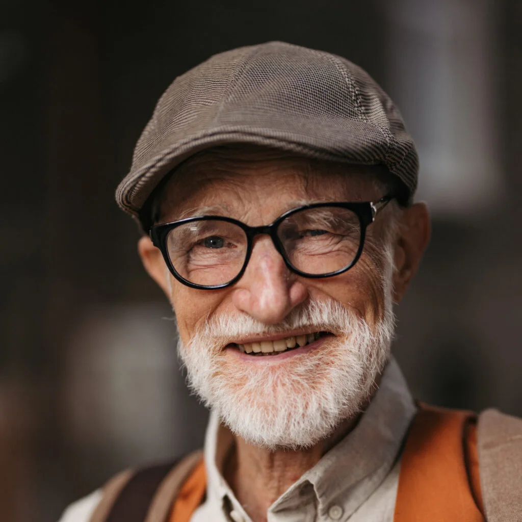 A man in his seventies wearing glasses and a flat cap, smiling